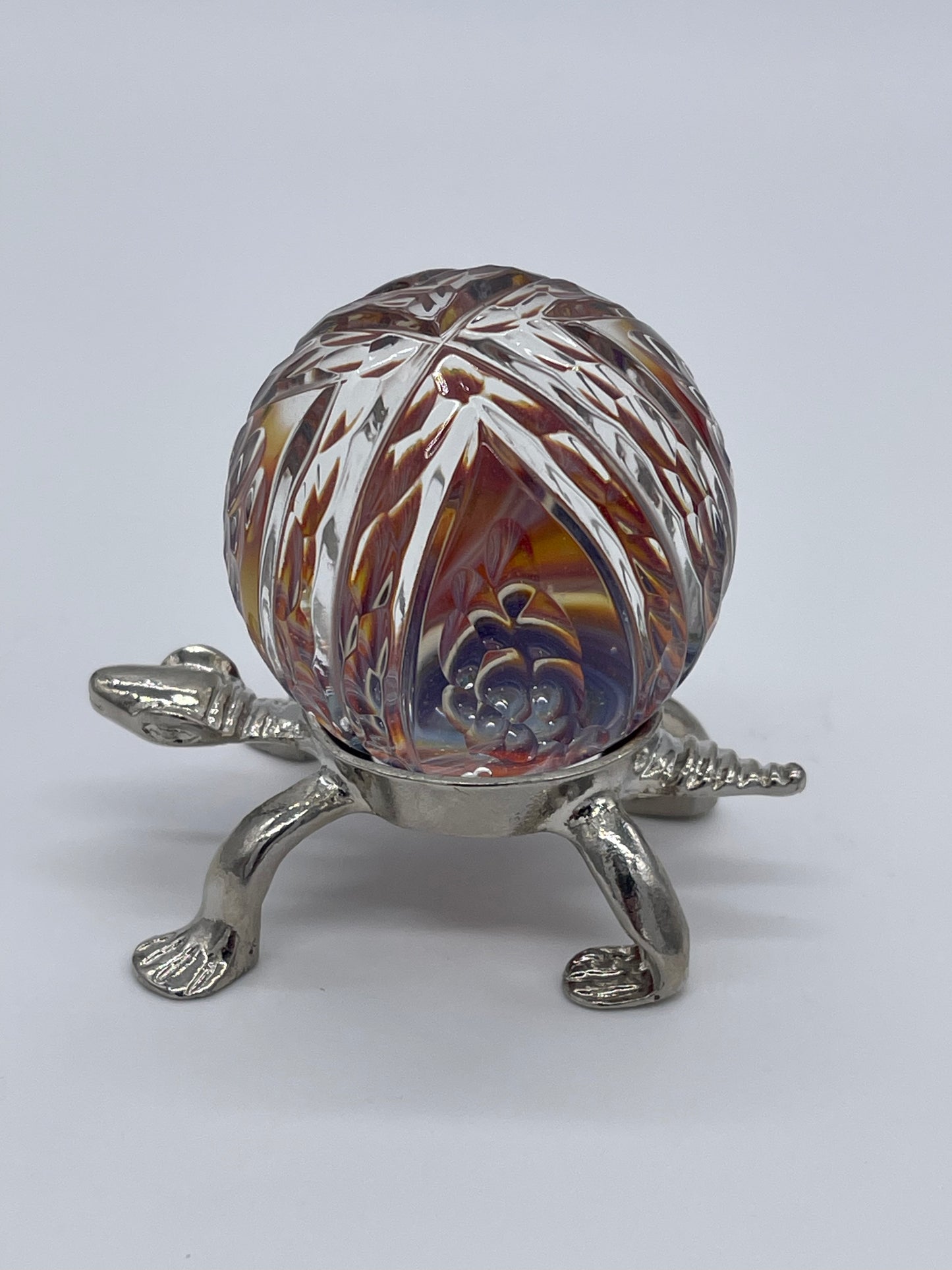 Take your glass game to the next level with American Marble's Ron Thomas 1.8 UV Faceted Marble! This bold and daring marble features American marble and Ron Thomas' signature UV faceting. Dare to go beyond ordinary marbles and elevate your collection with this unique piece. Turtle Holder Included with purchase !